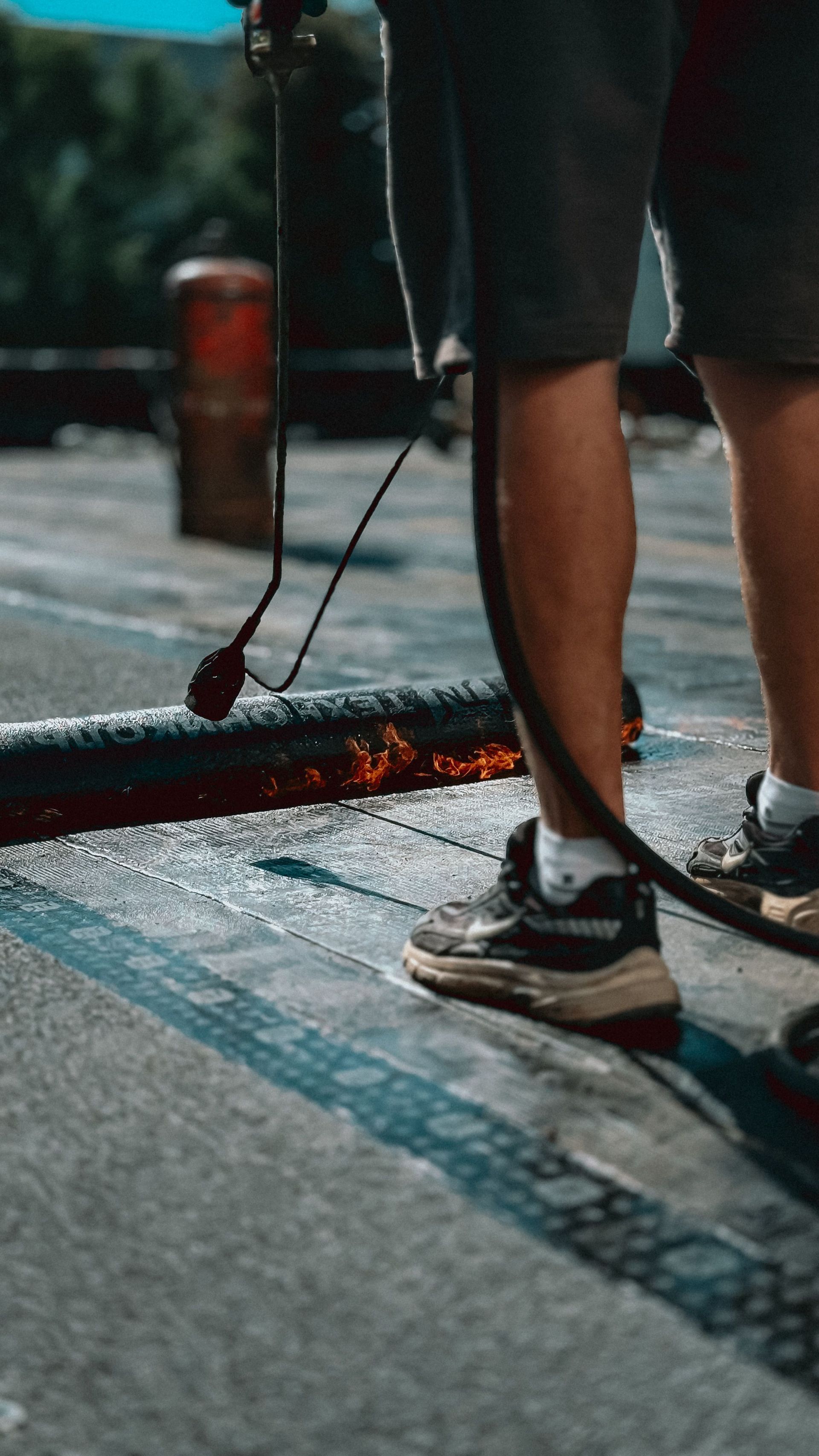 A laborer uses a flame torch to apply asphalt on a rooftop, showcasing construction skills.